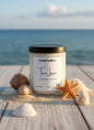 Candle labeled 'Tan Lines' on a wooden surface with ocean view